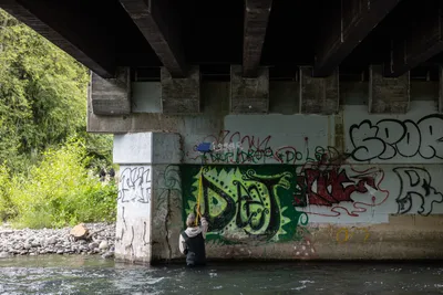 Friends including Jay Lundahl (painting with extension roller), Theresa Churchill (looking up), and others gather under a bridge to paint over hateful graffiti in Sequim, Washington on June 17, 2023.